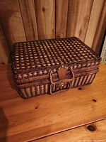 Closed vintage style wicker picnic basket with leather buckle and handle on wooden surface