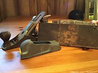 Photo shows multiple older woodworking hand planes including metal body planes and wooden planes on a wooden surface. Also shows several loose replacement blades.