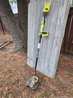 Full view of trimmer leaning against wooden fence