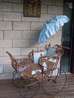 Front and side view of Victorian wicker baby carriage showing blue ruffled fabric canopy and cushion interior.