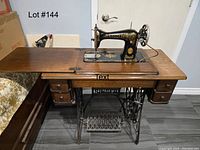 Full view of Singer sewing machine mounted in oak cabinet with fold-out leaves, drawers, and cast iron treadle stand.