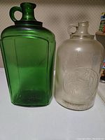 Photo of two glass jugs side by side on shelf; green BRIGHTS jug on left and clear LONDON WINERY LTD. jug on right.