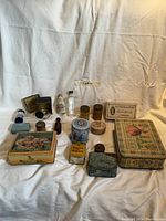 Photo showing assortment of antique tins and bottles including a decorative tin box with puppies, mustard tin, Laura Secord candy box, and various glass bottles and tins