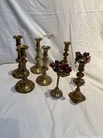 Photo showing all eight brass candle sticks arranged on a white backdrop, highlighting variations in design and decorative floral details on two sticks.