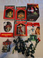 Photo showing 5 Christmas ornaments, 4 still inside original OrnaMotion packaging, one carousel ornament outside packaging, and 18 green rotating motor plugs bundled in the center