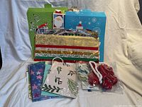 Various Christmas gift bags and sheets of wrapping paper arranged on a fabric background.
