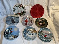 Front view of six collector plates featuring birds and winter landscapes along with two red woven mats.