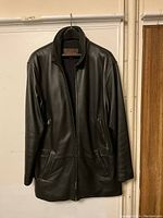 Front view of black leather men's coat on hanger, showing zippered front and pockets.
