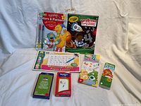 Photo shows a collection of children's educational materials including books, writing tablets, and card games arranged on a white surface.
