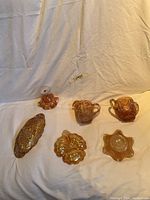 Front view of six carnival glass items arranged on white cloth, includes creamer, sugar bowl, candy dish, pedestal compote, honeycomb oval dish, and decorative bowl.