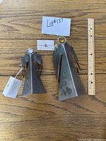 Photo of two steel angel sculptures placed on wooden surface with a ruler for scale and a business card.