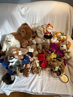 Front view of the lot showing a variety of teddy bears and plush toys with some original tags visible, arranged on a white blanket.