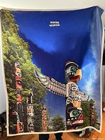 Fleece blanket displaying a printed image of Native totem poles, blue sky, and greenery, showing the texture and colors of the fabric.