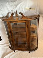 Front and top view of oak wall curio cabinet showing door, curved glass sides, shelves and decorative top finial.