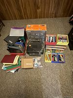 Overview of entire lot showing printers, folders/binders, writing instruments organized in containers, and printer ink box.