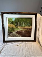 Front view of oil on canvas painting showing wooded landscape with water and framing details.