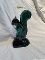 Side view of the glossy blue-green squirrel figurine standing upright with its large tail curved upwards on a base.