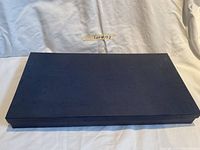 Closed box that contains the tray, navy blue with slight texture.