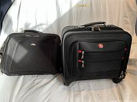 Two black carry bags sitting side by side against a white backdrop. On the left is a Samsonite over shoulder bag with a curved front and zipper. On the right is a Swiss Army rolling carry case with red zippers and handle, featuring the Swiss Army logo.