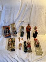 Full group of vintage figurine dolls, some loose, some in original packaging, on a fabric surface