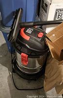 Side view of the vacuum showing stainless steel body, black top with red clip, hose attached.