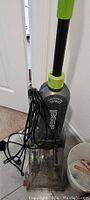 Full view of the Bissell upright carpet cleaner standing on floor with power cord wrapped around handle.
