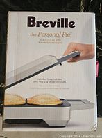 Front of box showing Breville branding, product name 'the Personal Pie,' image of pie maker in use with two pies visible on heated surface.