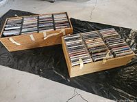 Two wooden cases filled with CDs placed on a tarp on the floor. Cases have some adhesive tape marks.