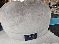 Close-up of the soft gray textured fabric pouf and the Chil-lax logo tag on the lower side.
