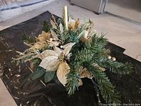 Top angled view of the Christmas centrepiece showing pine foliage, gold poinsettias, gold leaves and central candle.