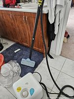 Full view of the Dupray rug steamer with hose extending to mop head on floor near bathroom cabinetry.