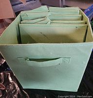 View of six green fabric storage bins stacked inside one another, showing front handle and fabric material.