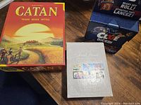 Top view of boxed Catan, Clue Diced, and Trivial Pursuit cards on a wooden surface.
