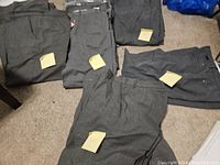 Five pairs of grey Holy Cross pants laid out on floor, some with size tags visible.