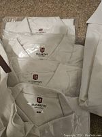 Five new white McCarthy brand uniform shirts size medium partially packaged, showing folded collars and tags.