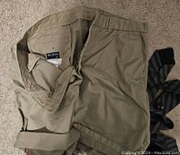 Pair of folded khaki shorts with a few ties placed beside them on a carpeted floor, showing the label inside the shorts and the belt loops.