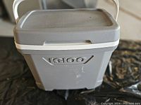 Front view of grey Igloo cooler with handle, showing the embossed Igloo logo on the front and slightly scuffed surface.
