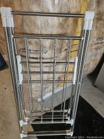Folded metal laundry drying rack with multiple horizontal bars and plastic joints for folding, standing vertically on ground