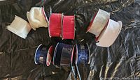 Photo showing several rolls of Christmas-themed wired ribbon in red, blue, white, and silver on a black surface.