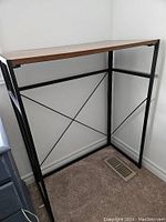 Clear angled photo of the empty standing computer table showing the wooden top and black metal frame with cross-bracing in a corner.