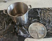 Stock pot next to its lid placed on a black plastic surface showing the inside and side of the pot