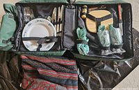 Open view of picnic set contents inside backpack including plates, cutlery, glasses, cheese board, shakers, napkins, and blanket.