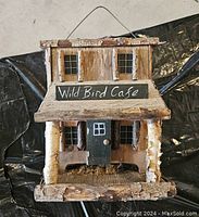 Front view of rustic hanging birdhouse featuring birch bark roof, two windows, a small door, and 'Wild Bird Cafe' sign.