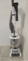 Full view of white and gray Shark Navigator Lift-Away upright vacuum cleaner with transparent dust cup showing dust inside, attached hose and floor head.