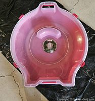 Top view of round pink wreath storage container showing integrating handle, red side latches, and molded internal supports for wreath.