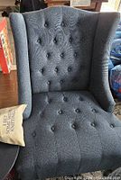 Blue tufted wing chair showing button tufting on seat and backrest with curved wings and dark detailing on legs.