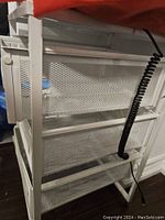 White metal wire storage unit with three mesh sliding drawers, showing side view of drawers and frame
