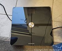 Top view of the Withings digital scale showing the full black glass surface with a central metal sensor and the Withings logo near the bottom edge.