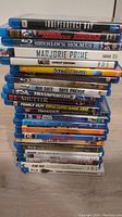 Stack of 26 Blu-ray movie cases showing titles and spines including Independence Day, Bangkok Dangerous, Sherlock Holmes, Saw II, Megamind, Due Date, Transporter 3, Family Guy, Hancock, Star Wars Lego, Clash of the Titans, Metal Gear Solid, The Last Exorcism, Stir Trek.