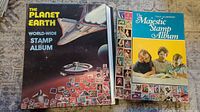 Photo showing two old stamp collector albums, The Planet Earth World-Wide Stamp Album and The Majestic Stamp Album arranged side by side.